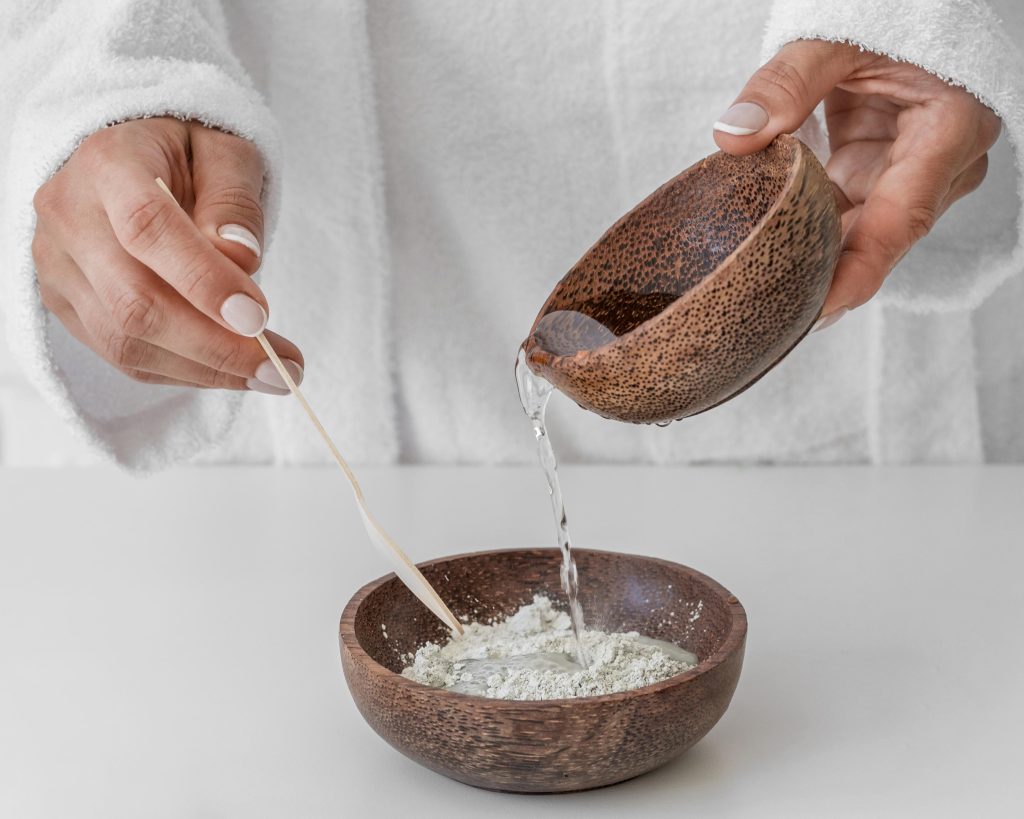 Дівчина у білому вбранні  змішує косметичну глину з водою