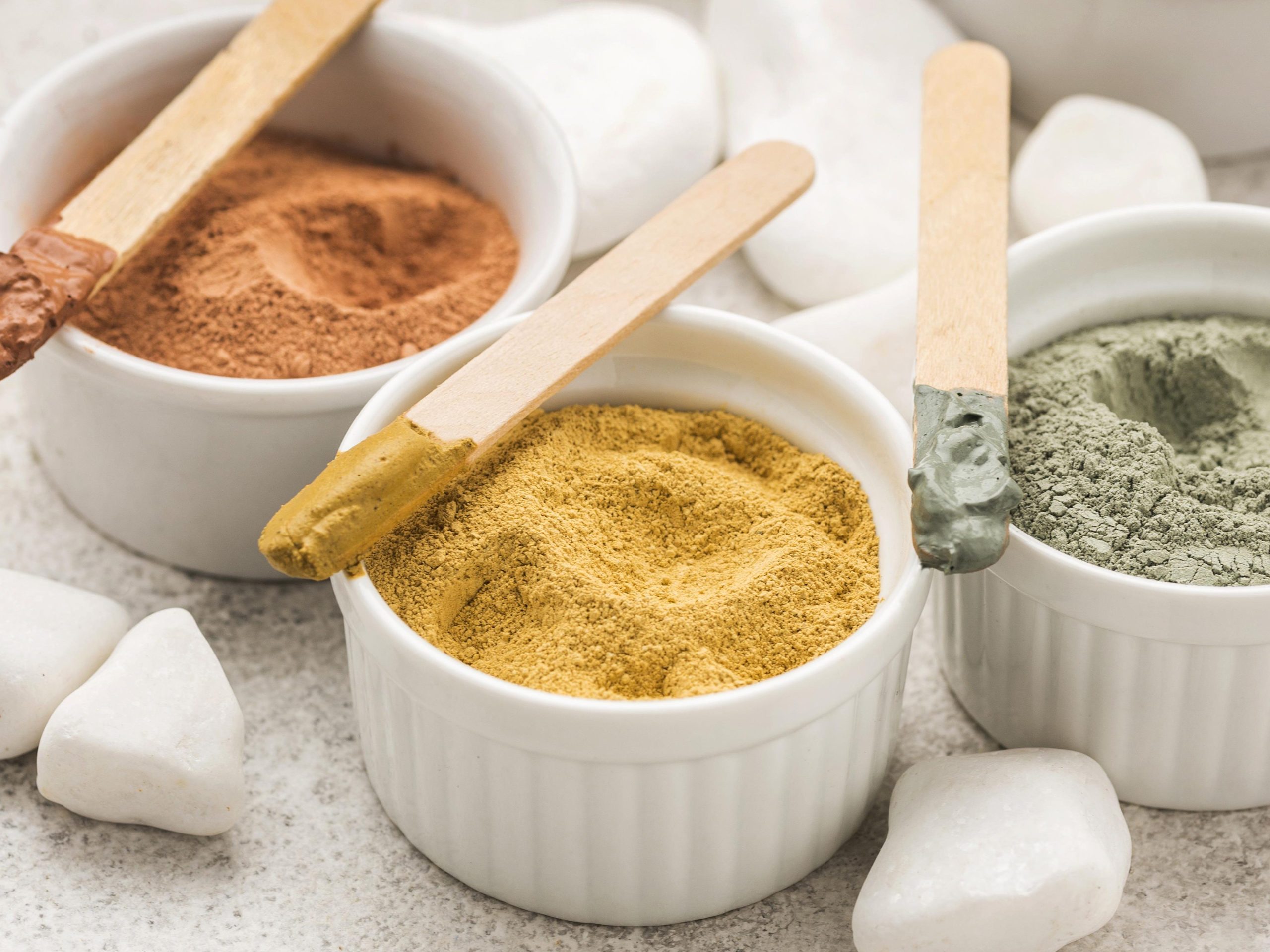 Виды косметической глины для лица в белой посуде с деревьяными палочками